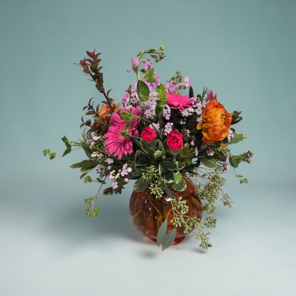 Mixed bouquet in an amber glass vase with pink, orange, and lavender flowers