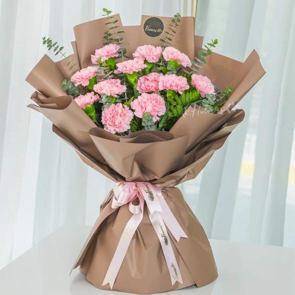 Pink carnation bouquet wrapped in brown paper with a ribbon