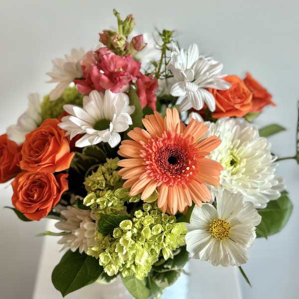 Mixed bouquet of orange roses, daisies, and pink blooms in a white vase