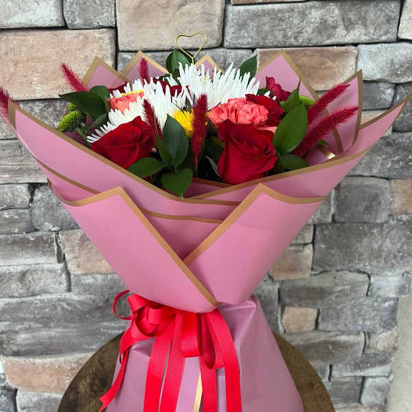 Bouquet of red roses, white chrysanthemums, and pink carnations wrapped in pink paper