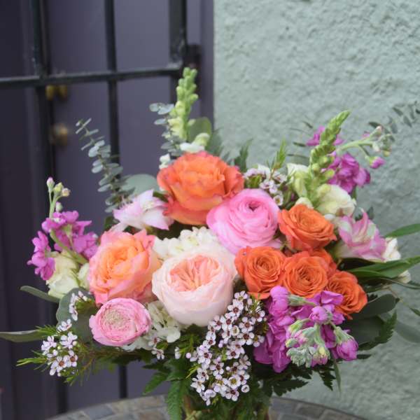 Mixed bouquet of pink and orange roses and other flowers in a clear glass vase