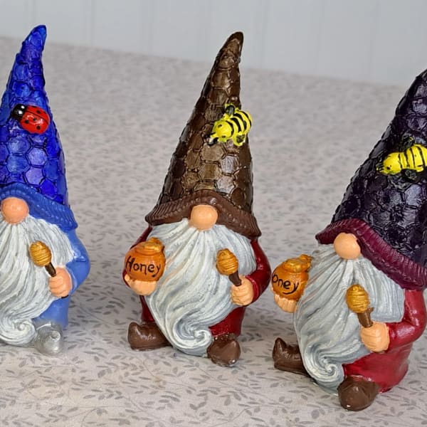 Set of four colorful gnome figurines holding honey pots with bees and a ladybug on their tall textured hats.