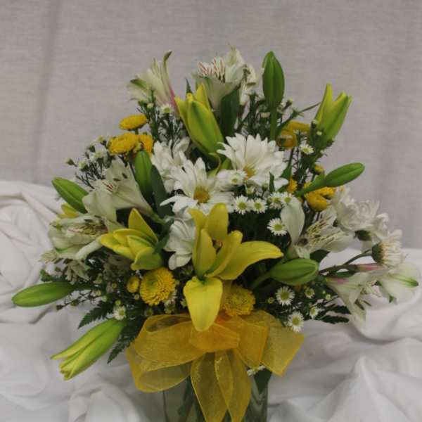 Yellow lilies and white daisies in a glass vase with a yellow ribbon