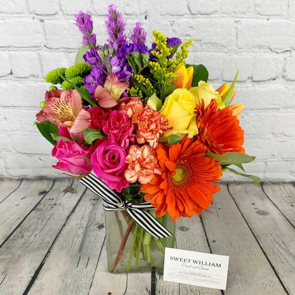 Colorful mixed bouquet in a glass vase with a striped ribbon