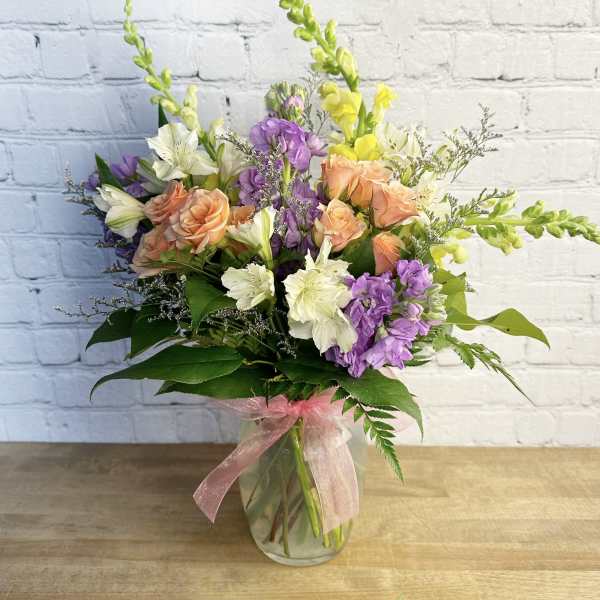 Mixed bouquet of peach roses, purple flowers, and white blooms in a glass vase