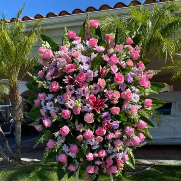 Tall pink and lavender standing spray with roses, lilies, and carnations on a wooden easel outdoors