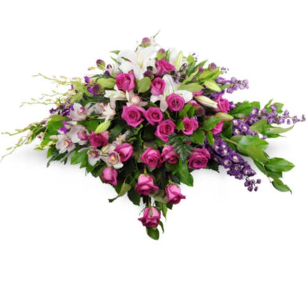 Casket spray of pink roses, white lilies, and purple flowers in a low, elongated design
