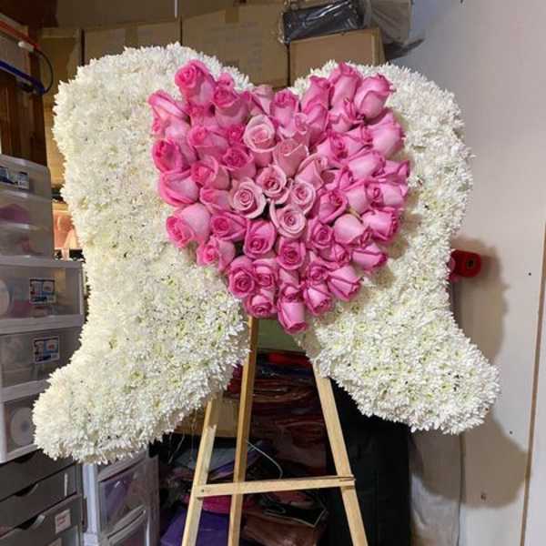 Standing white angel wings floral display with pink rose heart on a wooden easel