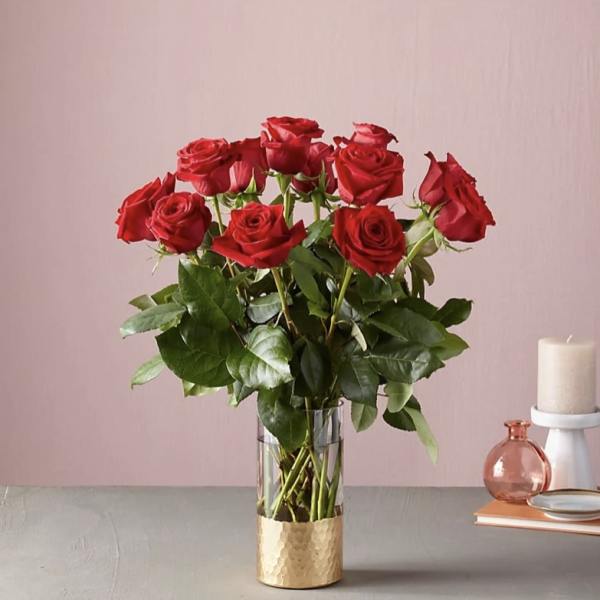 Red roses arranged in a clear glass vase with a gold base