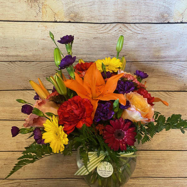 Colorful mixed bouquet in a clear glass vase with lilies and daisies