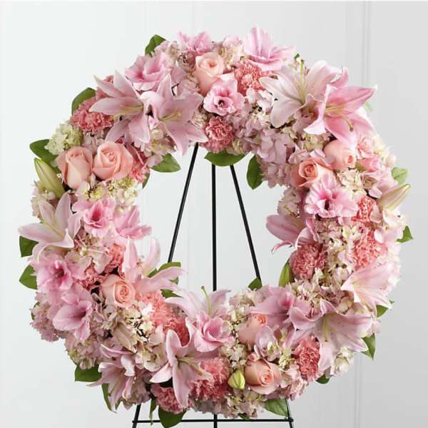 Pink floral wreath with lilies, roses, and carnations on a black stand