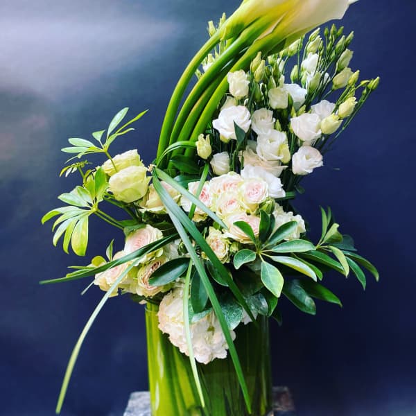 Tall white floral arrangement with calla lilies and roses in a glass vase