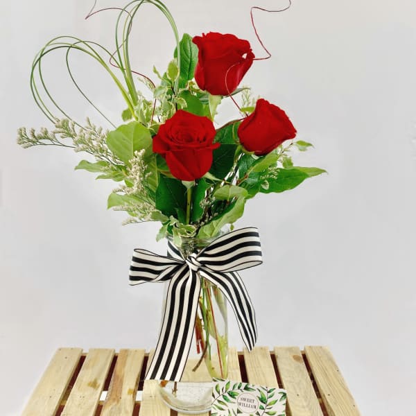 Three red roses in a clear glass vase with a striped bow
