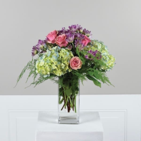 Bouquet of pink roses and purple flowers in a clear glass vase