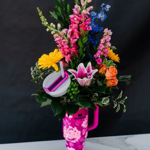 Colorful flower arrangement in a pink tumbler with a straw