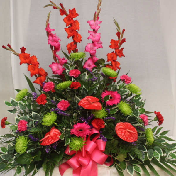 Tall floral spray with red and pink blooms and a bright pink ribbon