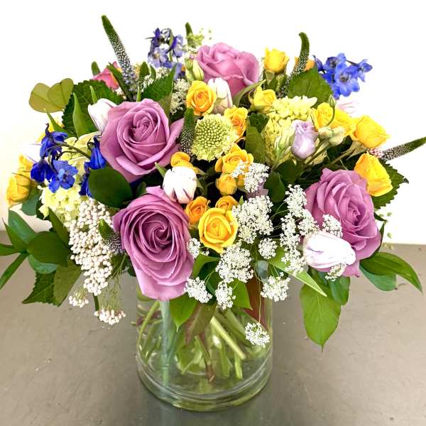 Mixed bouquet of purple, yellow, and blue flowers in a glass vase