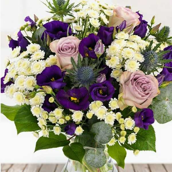 Bouquet of purple and blush roses with white daisies in a glass vase