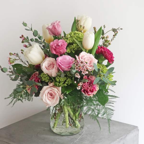 Bouquet of pink roses, white tulips, and carnations in a glass vase