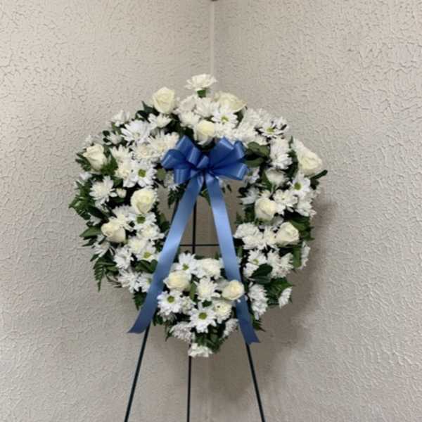 White floral funeral wreath on a stand with a blue ribbon