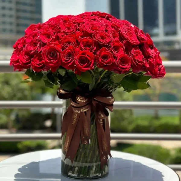 Large bouquet of red roses in a glass vase with a brown ribbon