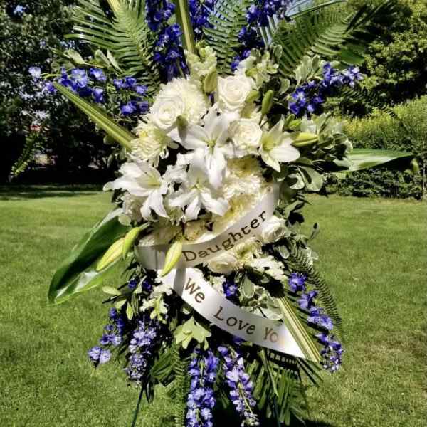 Standing floral spray with white lilies and purple flowers on an easel