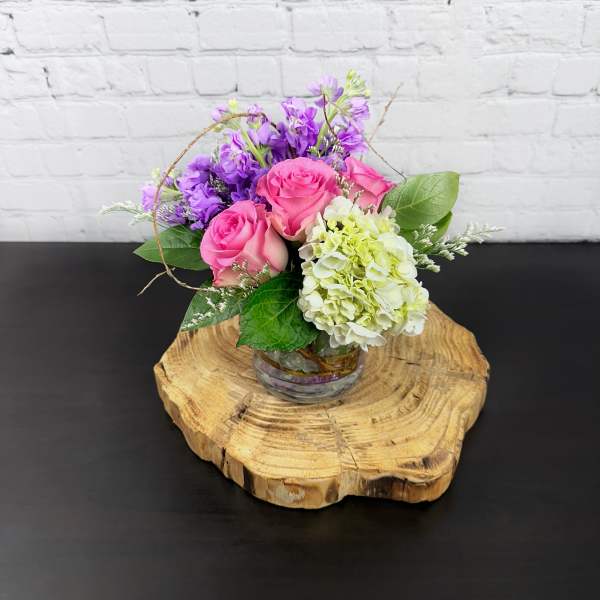 Pink roses and purple flowers arranged in a small glass vase
