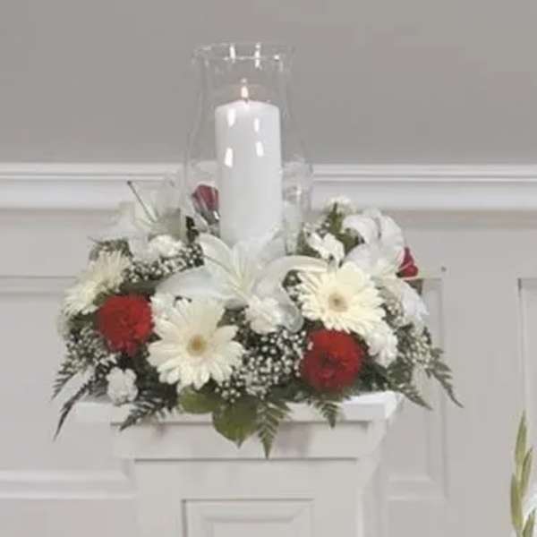 White candle in a glass hurricane surrounded by red and white flowers