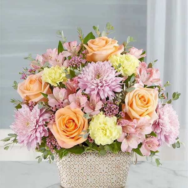 Peach roses and pink flowers arranged in a patterned basket