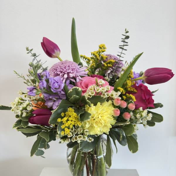 Colorful mixed bouquet with pink roses, yellow carnation, tulips and lavender blooms in a clear glass vase