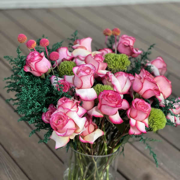 Pink roses arranged in a clear glass vase with green pom-pom accents.