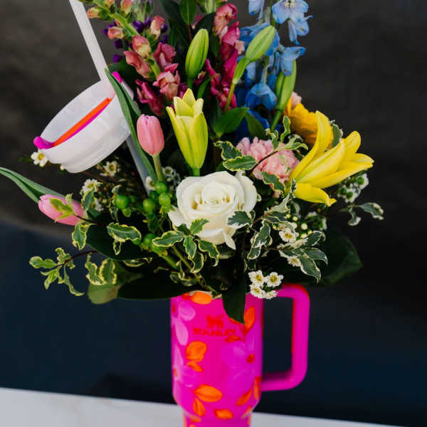 Mixed bouquet in a bright pink handled tumbler with lilies, roses, and snapdragons