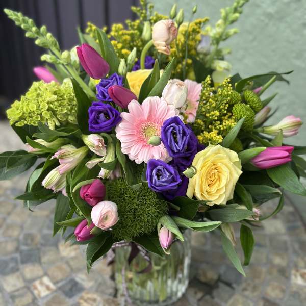 Vase arrangement of pink tulips, purple lisianthus, a yellow rose and mixed blooms in a clear glass vase.