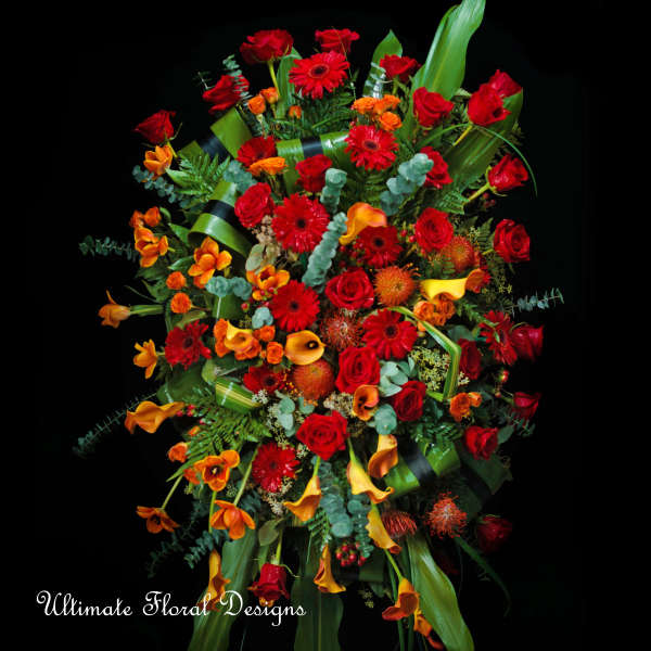 Large bouquet of red and orange flowers with green foliage on a black background
