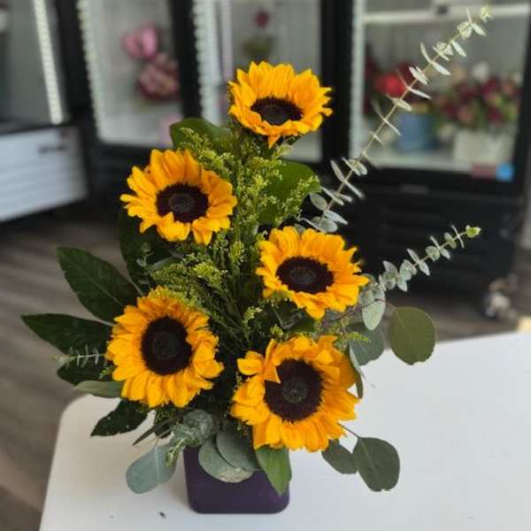 Sunflower arrangement in a purple vase with eucalyptus accents