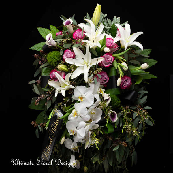 Large funeral spray with white lilies, orchids, and pink roses on a black ribbon