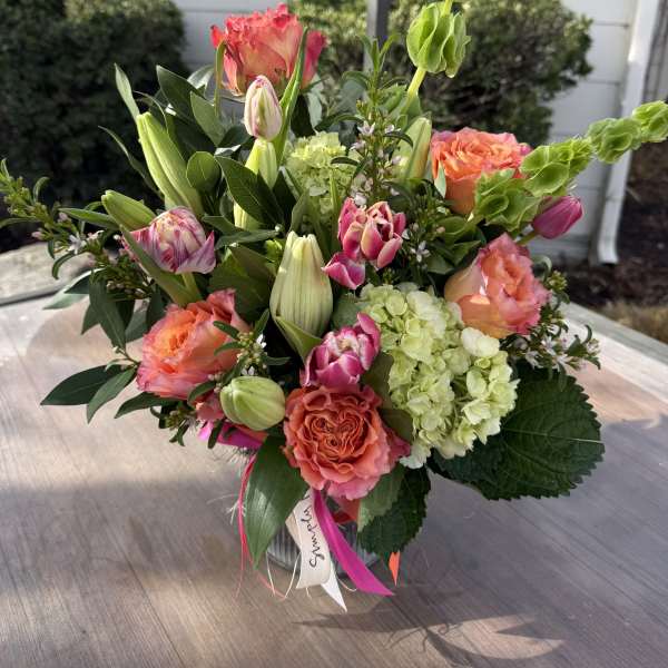 Mixed bouquet of coral roses, pink tulips, green hydrangeas, and lilies in a clear glass vase.