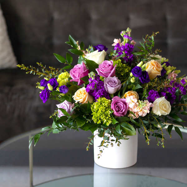 Mixed bouquet of roses and purple blooms in a white vase