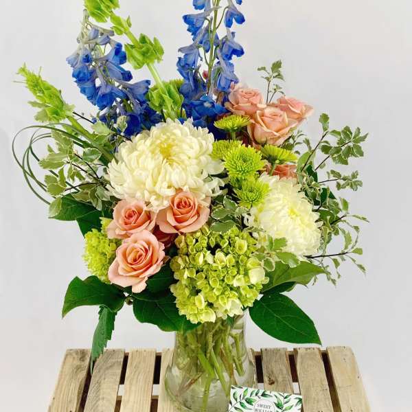 Mixed bouquet in a glass vase with blue delphinium, peach roses, and white chrysanthemums