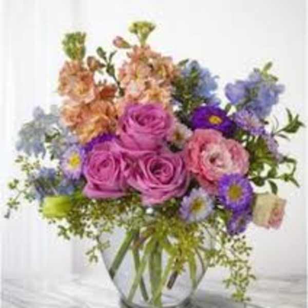 Mixed bouquet of pink roses and purple flowers in a clear glass vase