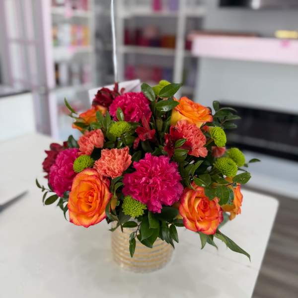 Bouquet of orange roses, pink carnations, and green button mums in a glass vase