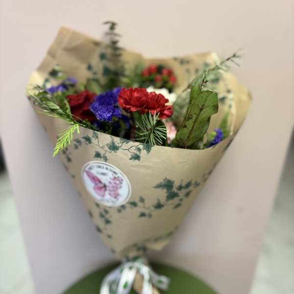 Wrapped bouquet of red and purple flowers with greenery