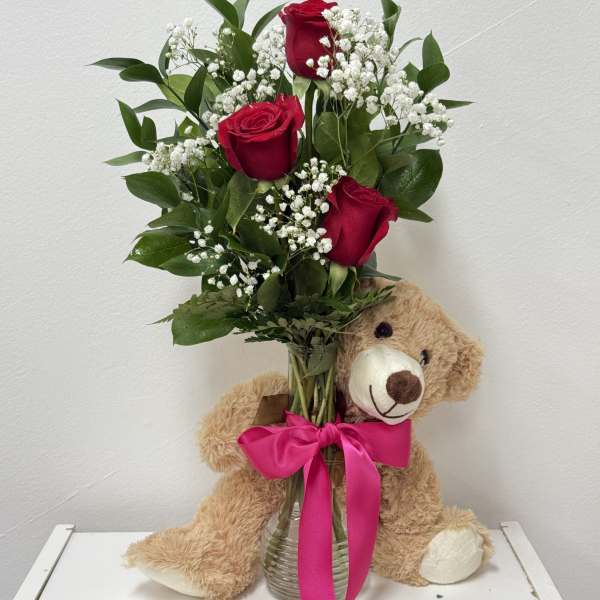 Red roses in a glass vase with a teddy bear and pink ribbon