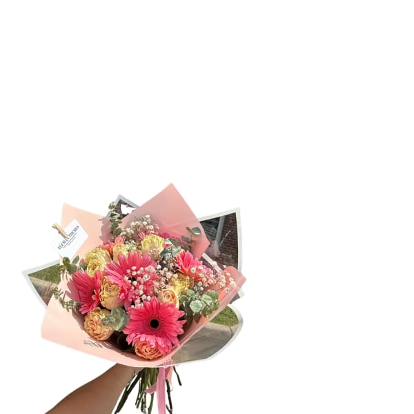 Handheld bouquet of pink gerbera daisies and peach roses wrapped in pink paper