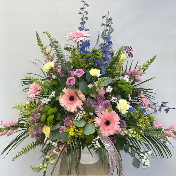 Large mixed floral arrangement with pink gerberas and blue delphinium in a white vase