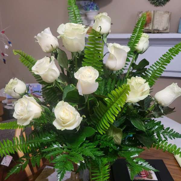 White roses arranged with fern foliage in a clear vase