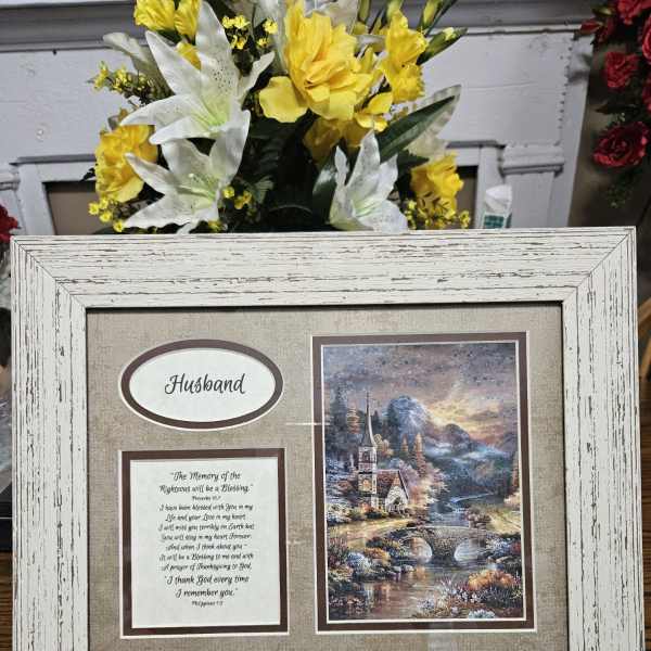 Framed memorial display with yellow and white flowers behind it