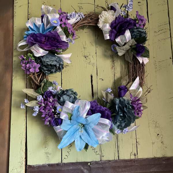 Heart-shaped floral wreath with purple and blue flowers and ribbon