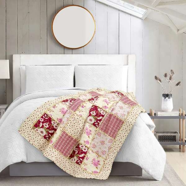 Patchwork quilt draped over a white bed in a bright bedroom