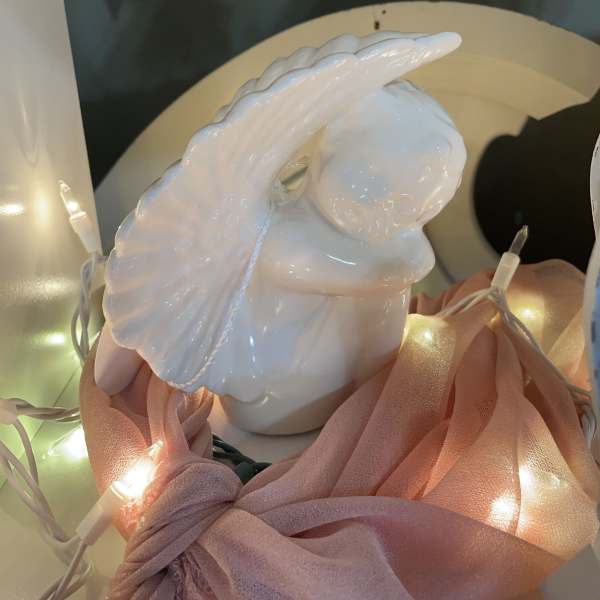 White ceramic angel figurine with pink fabric and string lights
